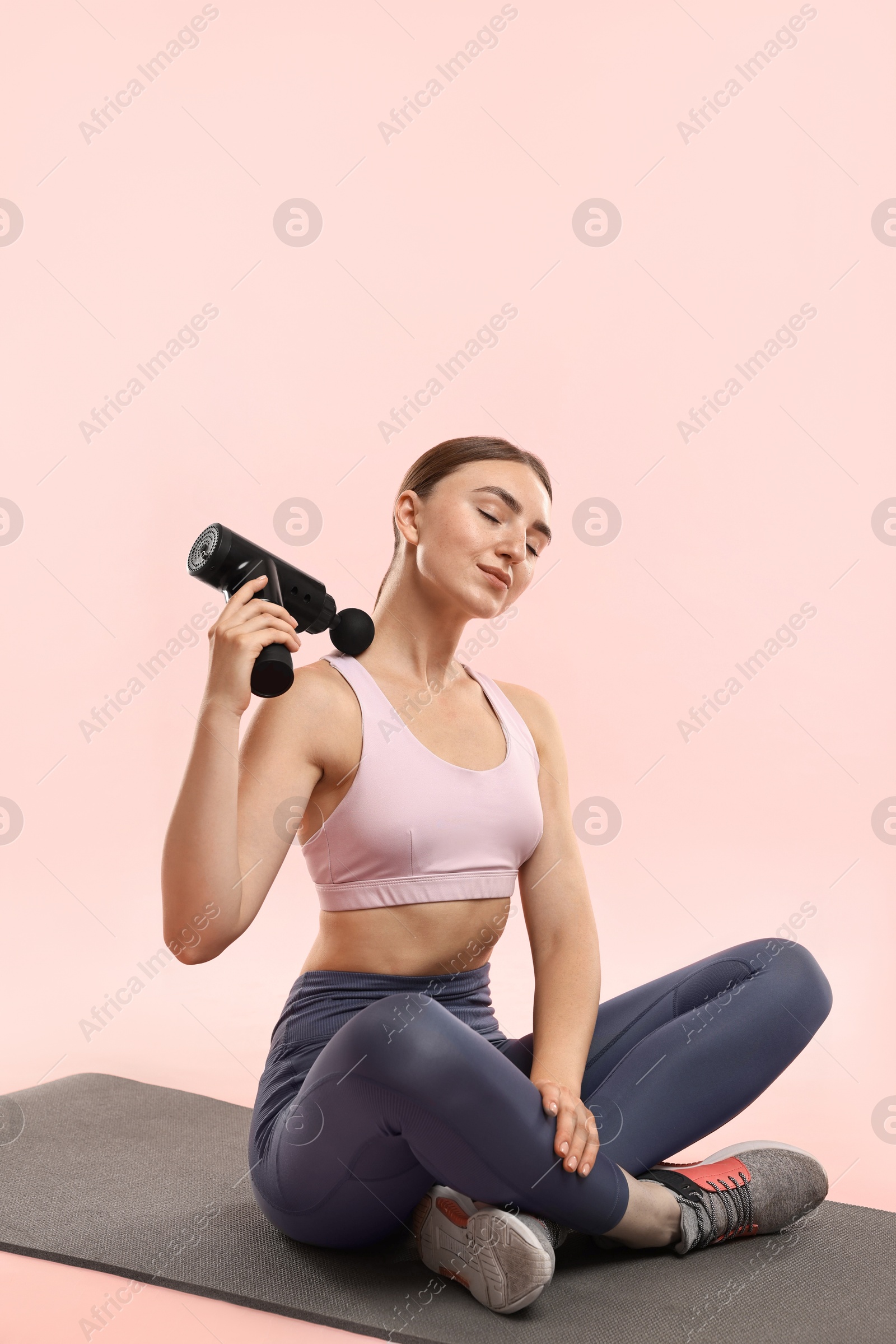 Photo of Woman using percussive massager to relieve trapezius muscle on pink background