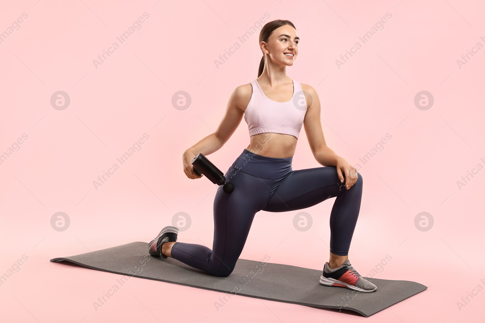 Photo of Woman using percussive massager to relax hip muscles on mat against pink background