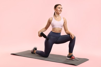 Photo of Woman using percussive massager to relax hip muscles on mat against pink background