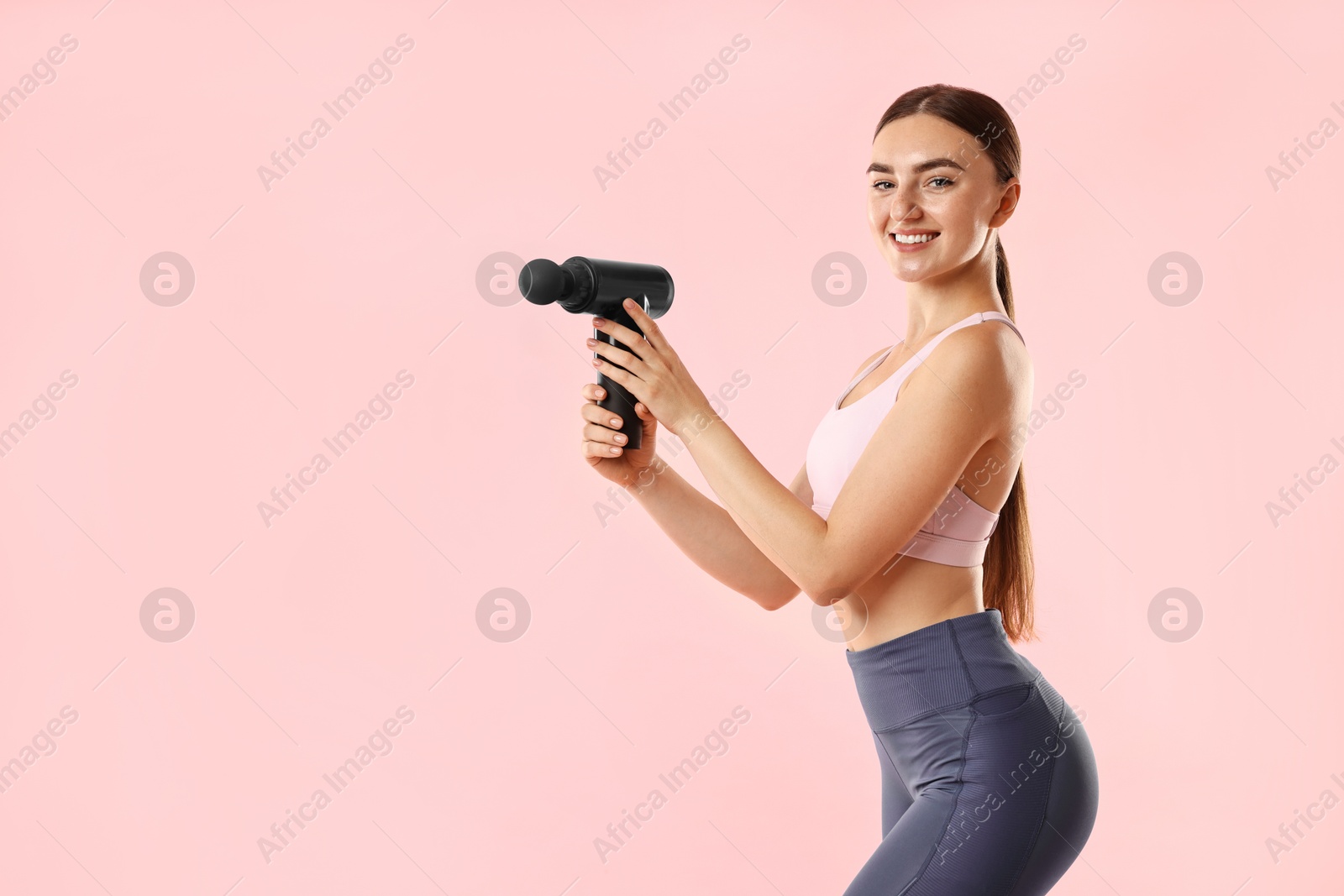 Photo of Young woman with percussive massager on pink background. Space for text