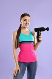 Young woman with percussive massager on light purple background