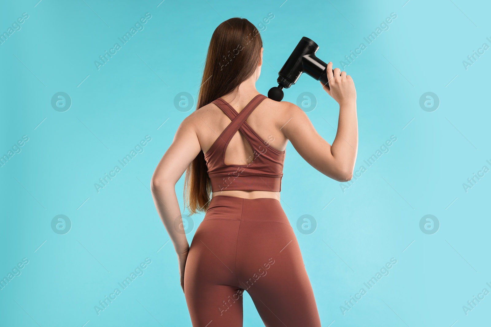 Photo of Woman using percussive massager to relieve trapezius muscle on light blue background, back view