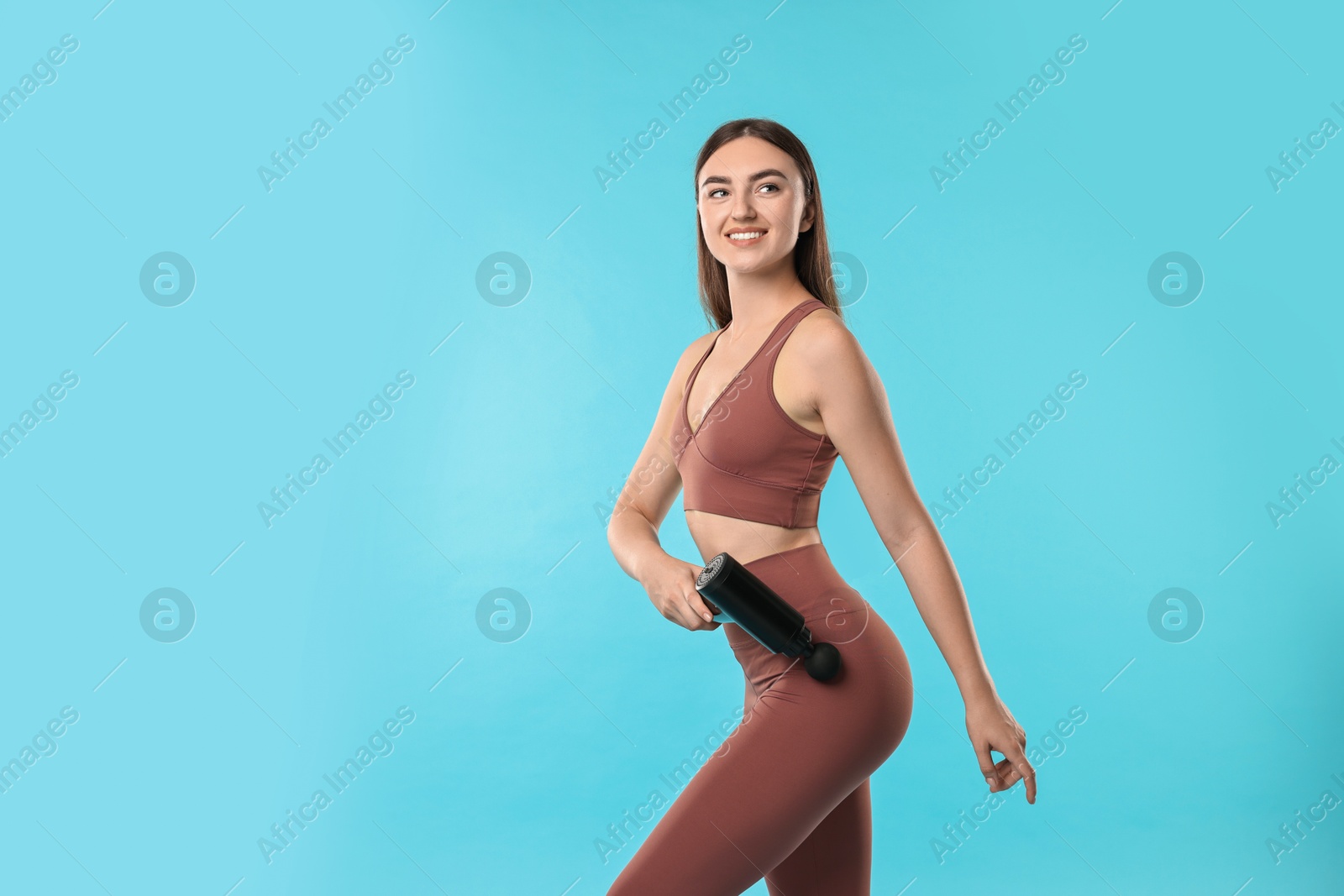 Photo of Woman using percussive massager to relax hip muscles on light blue background. Space for text