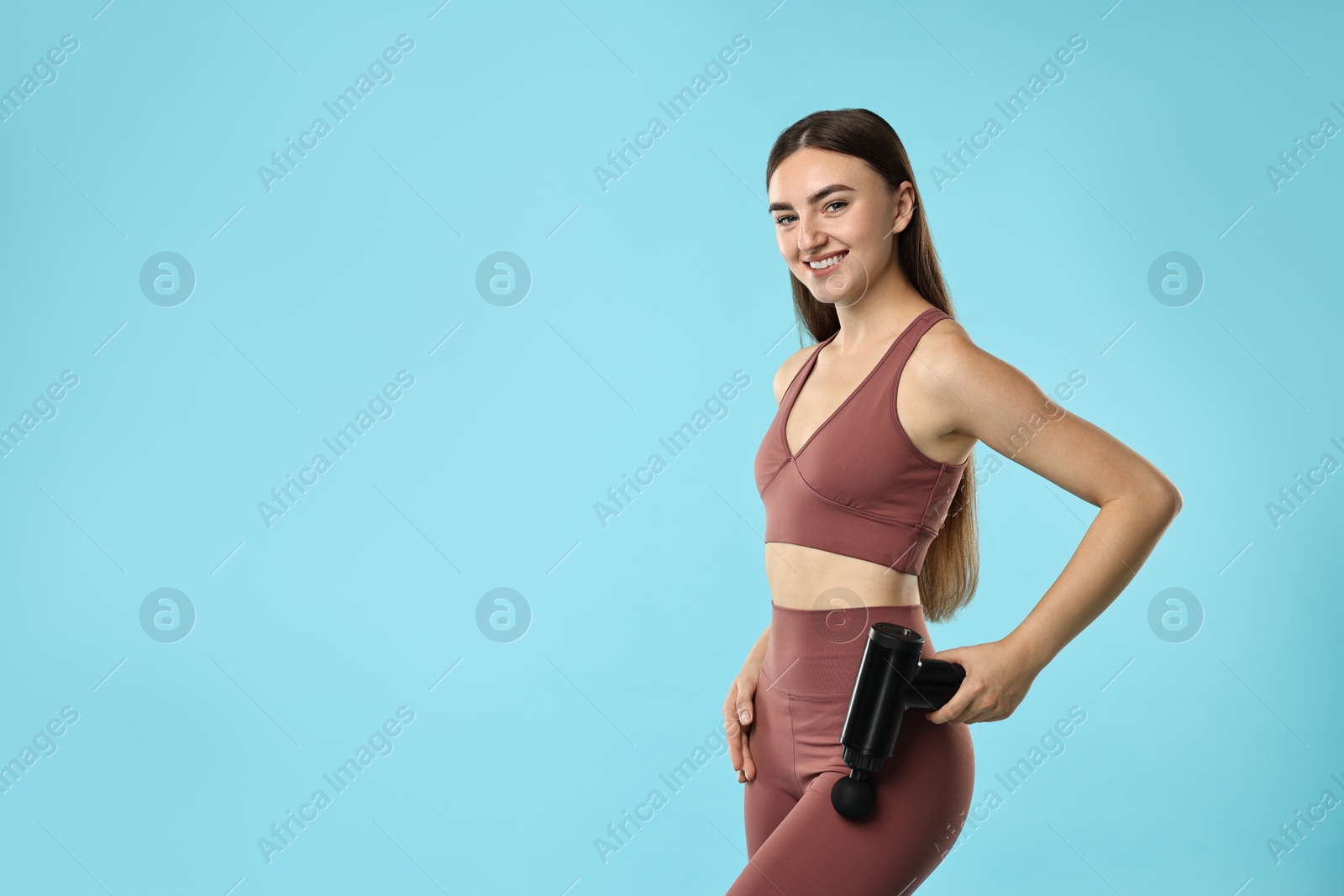 Photo of Woman using percussive massager to relax hip muscles on light blue background. Space for text