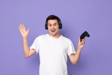 Photo of Happy young man in headphones with controller on violet background