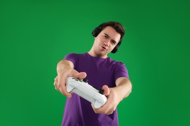 Young man in headphones playing video games with controller on green background