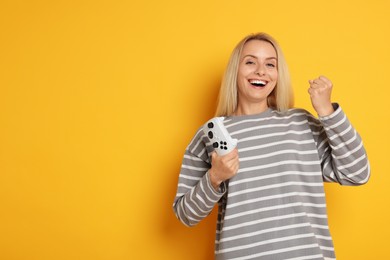 Happy woman with controller on orange background, space for text