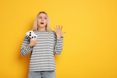 Unhappy woman with controller on orange background, space for text