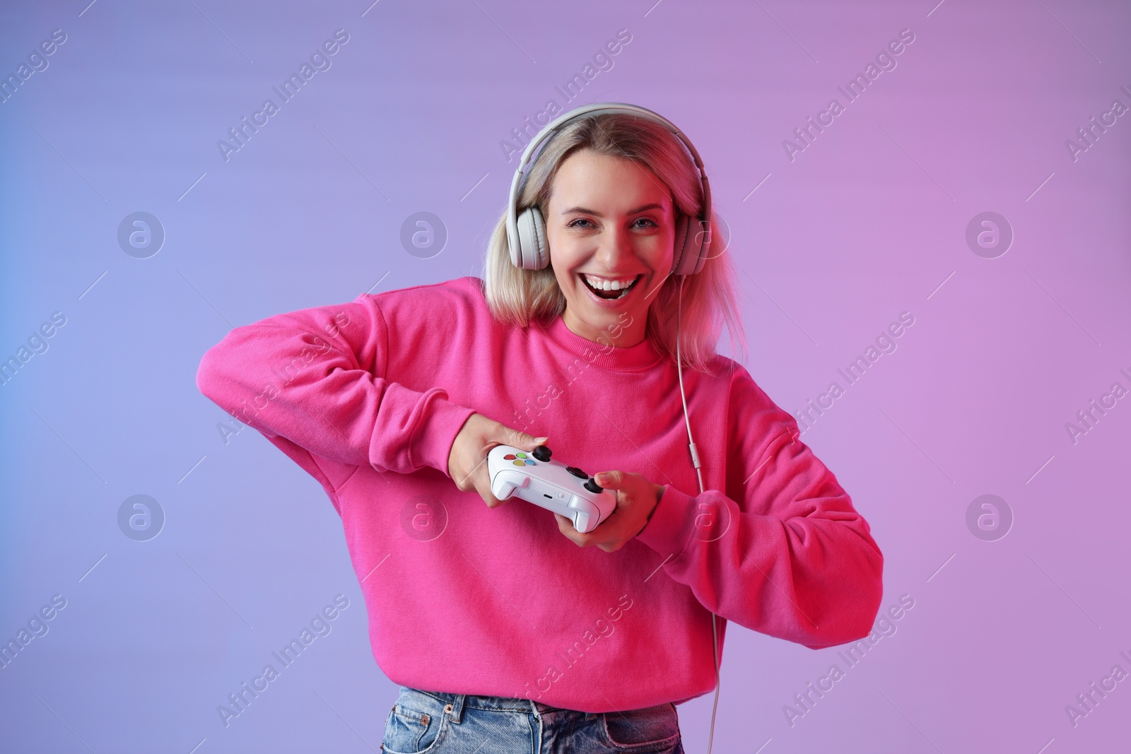 Photo of Happy woman in headphones playing video games with controller on color background