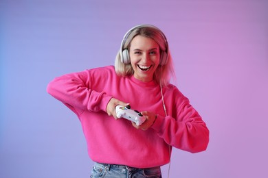 Happy woman in headphones playing video games with controller on color background