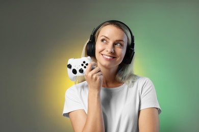 Happy woman in headphones with controller on color background