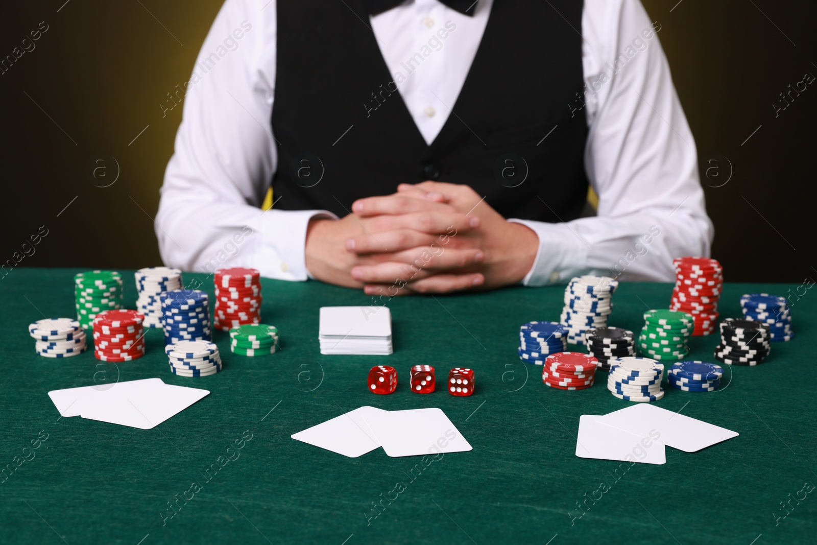 Photo of Professional croupier at gambling table with playing cards, casino chips and dice, closeup