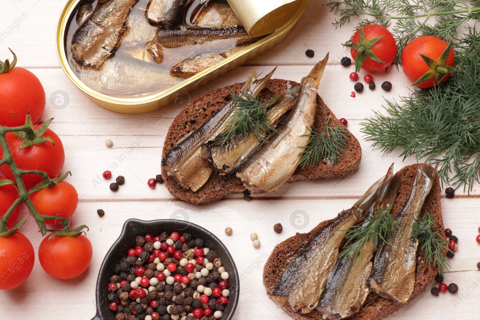 Photo of Delicious sandwiches with sprats and dill served on white wooden table, flat lay