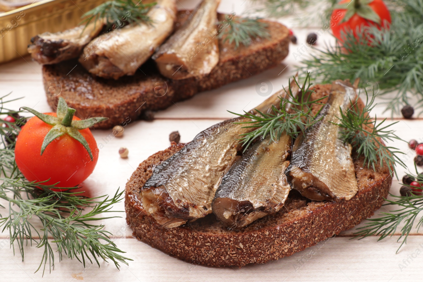 Photo of Delicious sandwiches with sprats and dill served on white wooden table, closeup