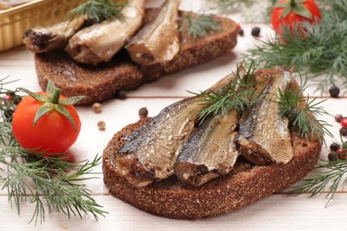 Delicious sandwiches with sprats and dill served on white wooden table, closeup