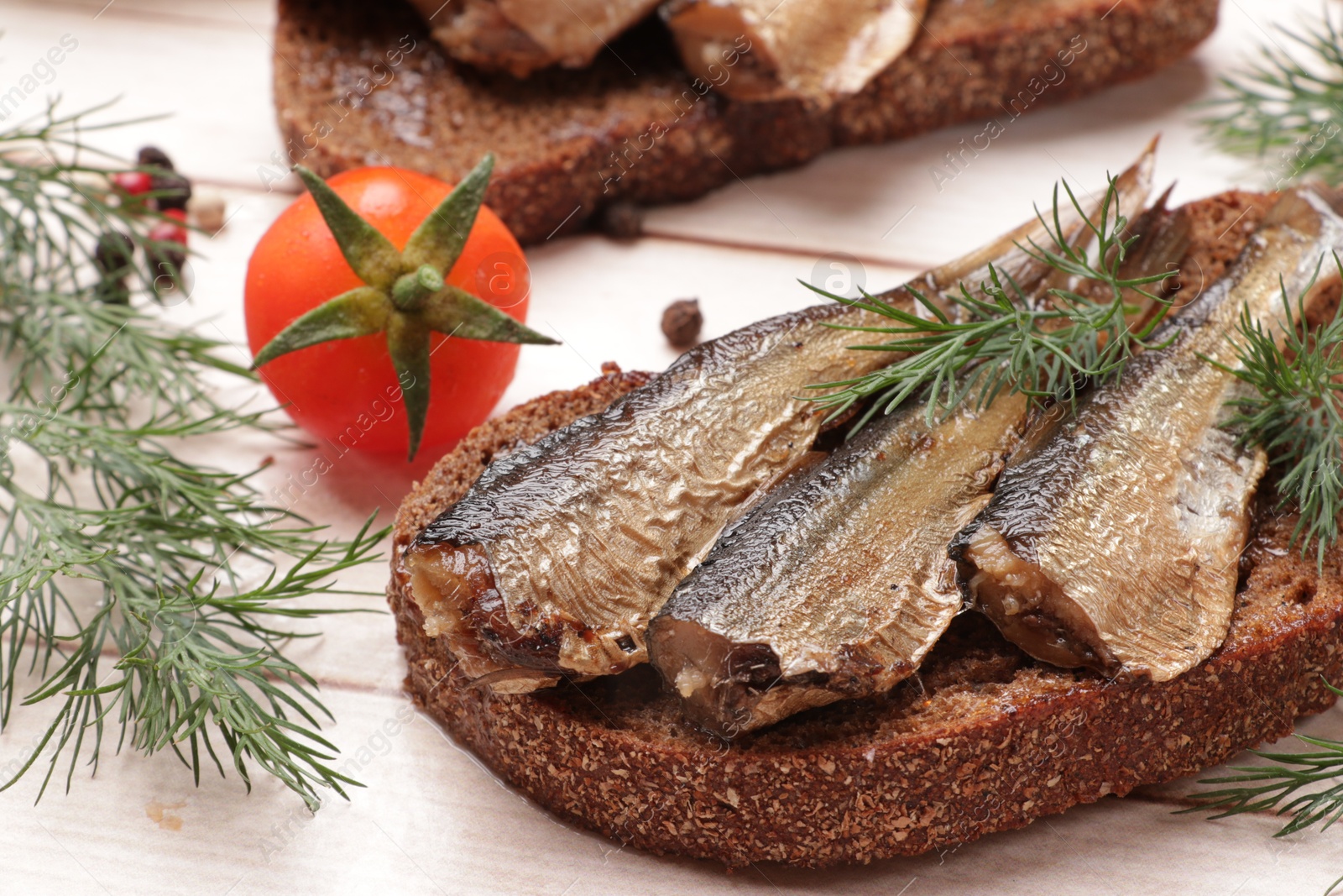 Photo of Delicious sandwich with sprats, dill and tomato on white wooden table, closeup