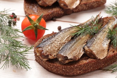 Photo of Delicious sandwich with sprats, dill and tomato on white wooden table, closeup