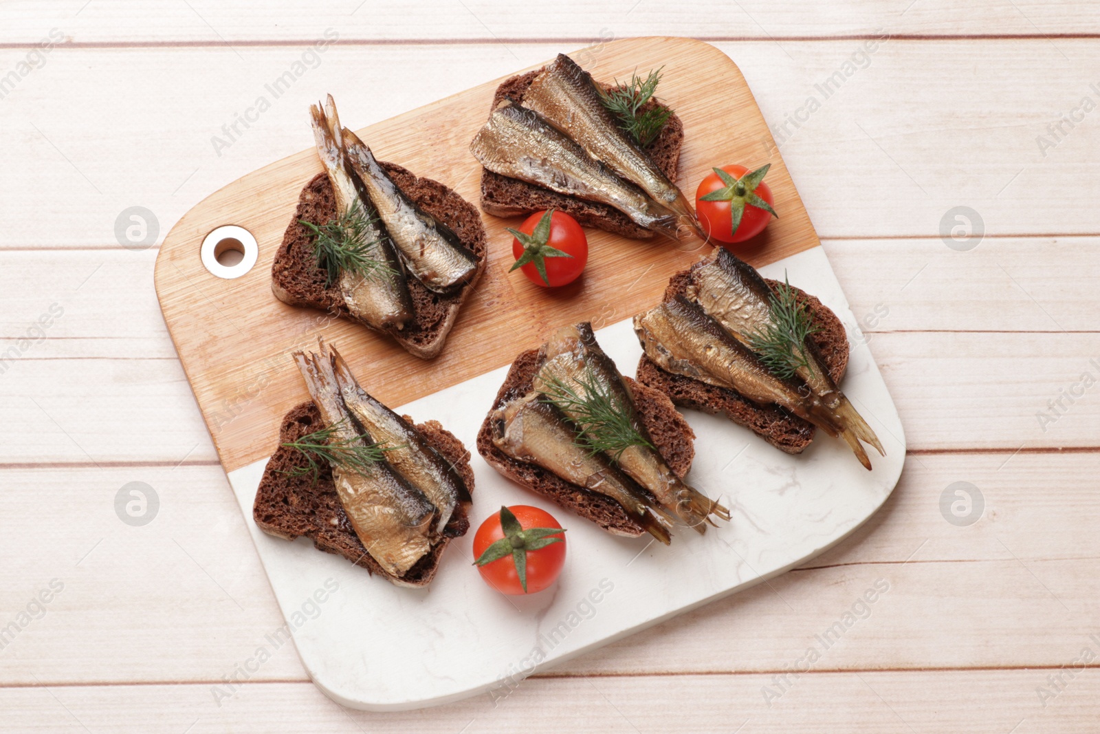 Photo of Delicious sandwiches with sprats, dill and tomatoes on white wooden table, top view