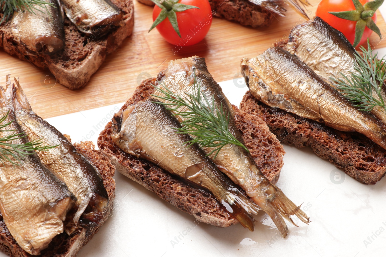 Photo of Delicious sandwiches with sprats, dill and tomatoes on table, closeup