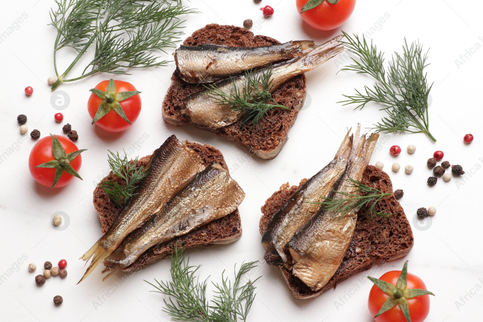 Photo of Delicious sandwiches with sprats, dill, tomatoes and peppercorns on white table, flat lay