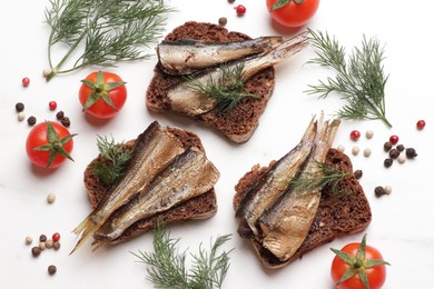 Photo of Delicious sandwiches with sprats, dill, tomatoes and peppercorns on white table, flat lay