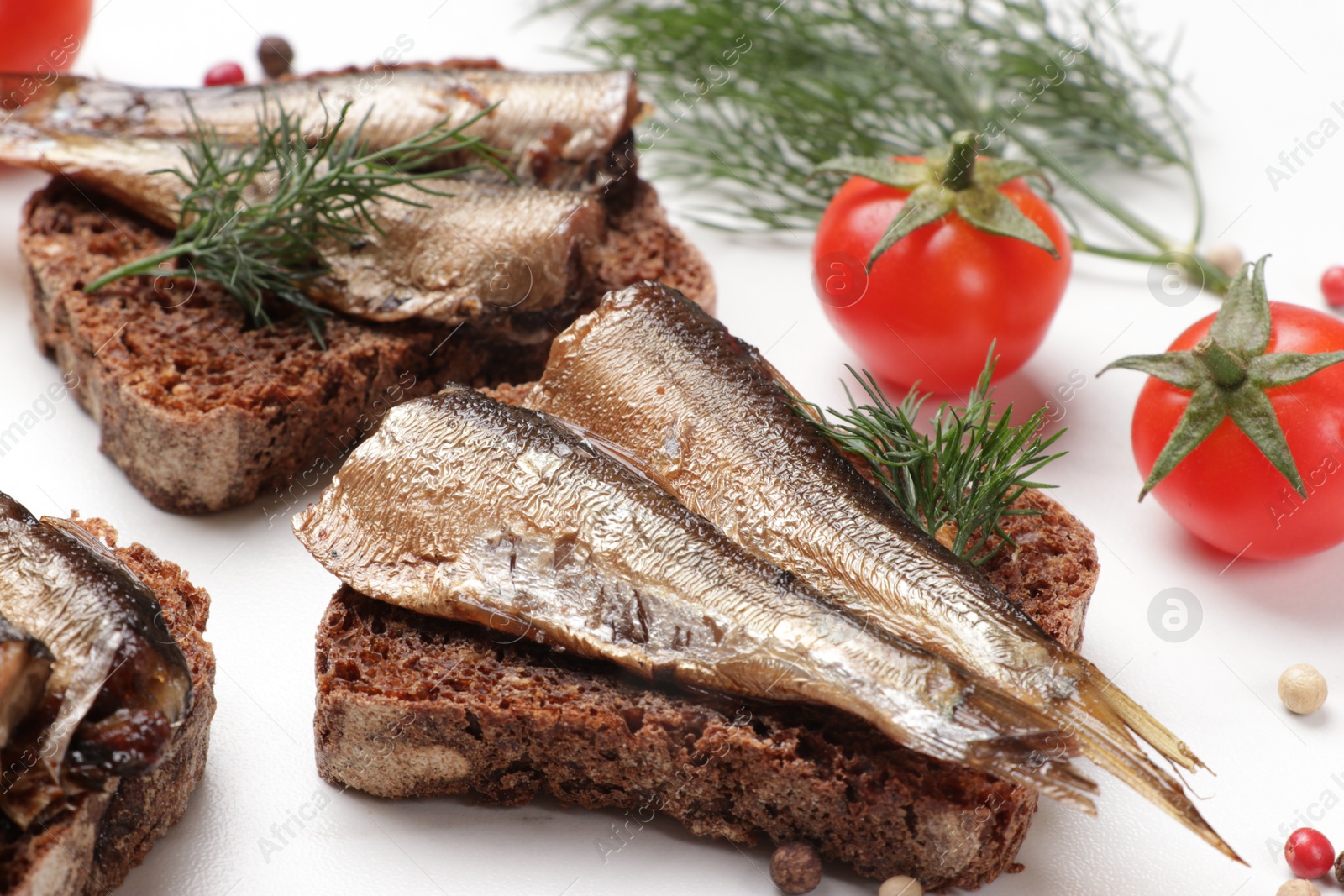 Photo of Delicious sandwiches with sprats, dill, tomatoes and peppercorns on white table, closeup