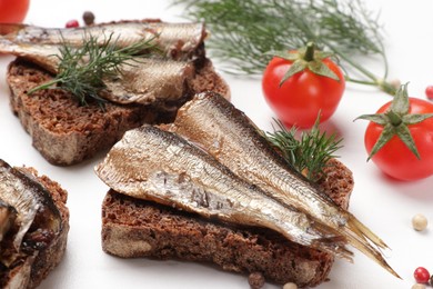 Delicious sandwiches with sprats, dill, tomatoes and peppercorns on white table, closeup