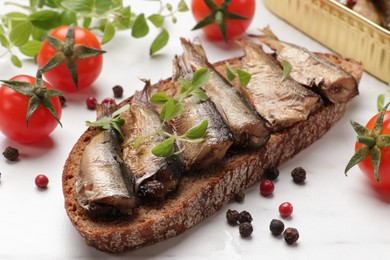 Delicious sandwich with sprats, microgreens, tomatoes and peppercorns on white table, closeup