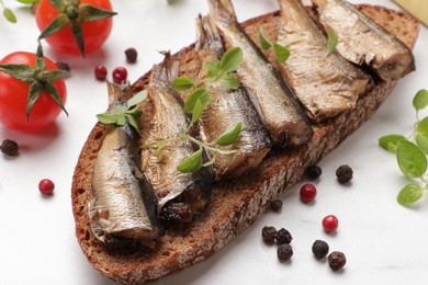 Delicious sandwich with sprats, microgreens, tomatoes and peppercorns on white table, closeup