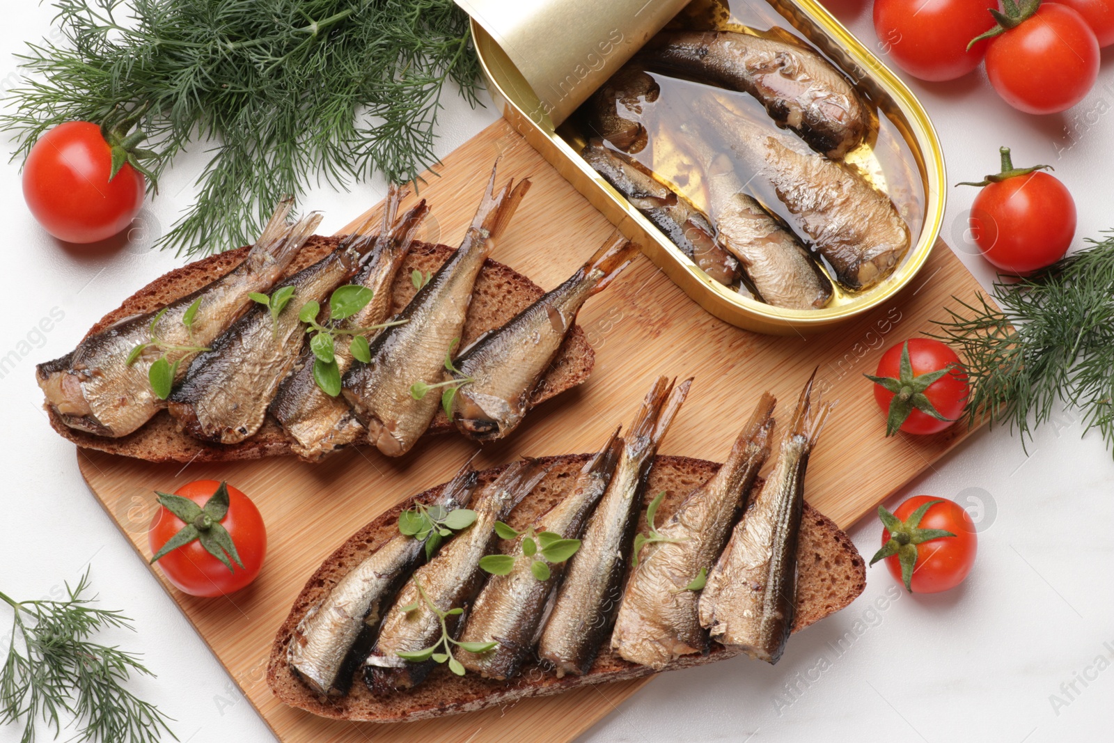 Photo of Delicious sandwiches with sprats, dill and tomatoes on white table, top view