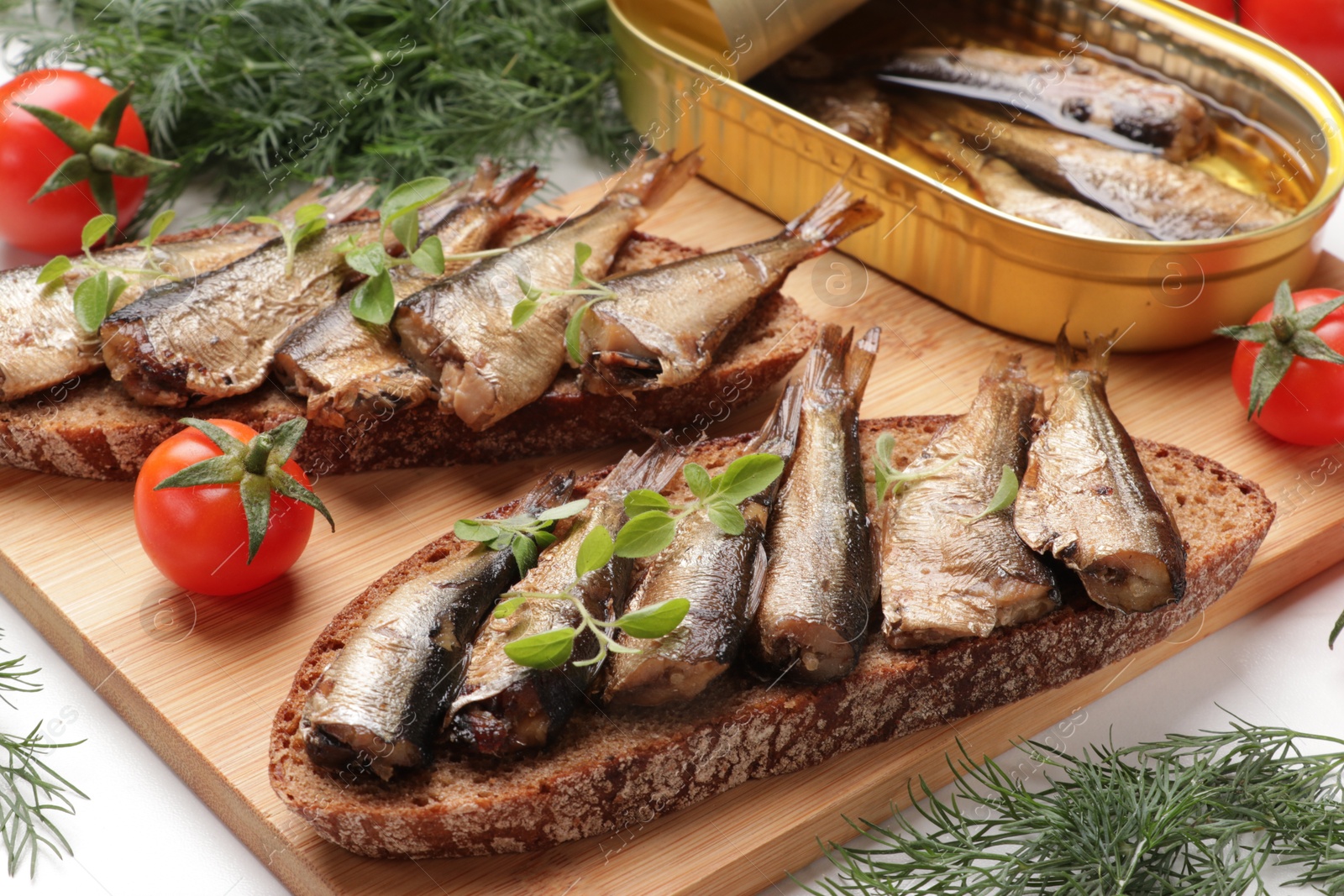 Photo of Delicious sandwiches with sprats, dill and tomatoes on white table, closeup