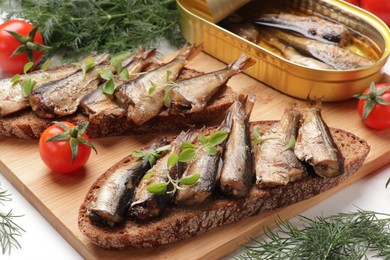 Photo of Delicious sandwiches with sprats, dill and tomatoes on white table, closeup