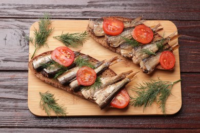 Delicious sandwiches with sprats, dill and tomato on wooden table, top view