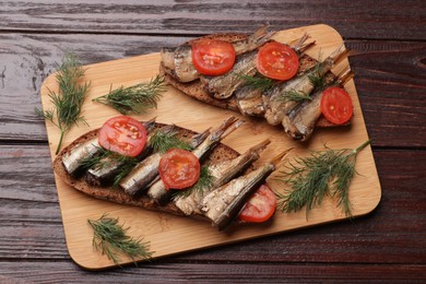 Delicious sandwiches with sprats, dill and tomato on wooden table, top view