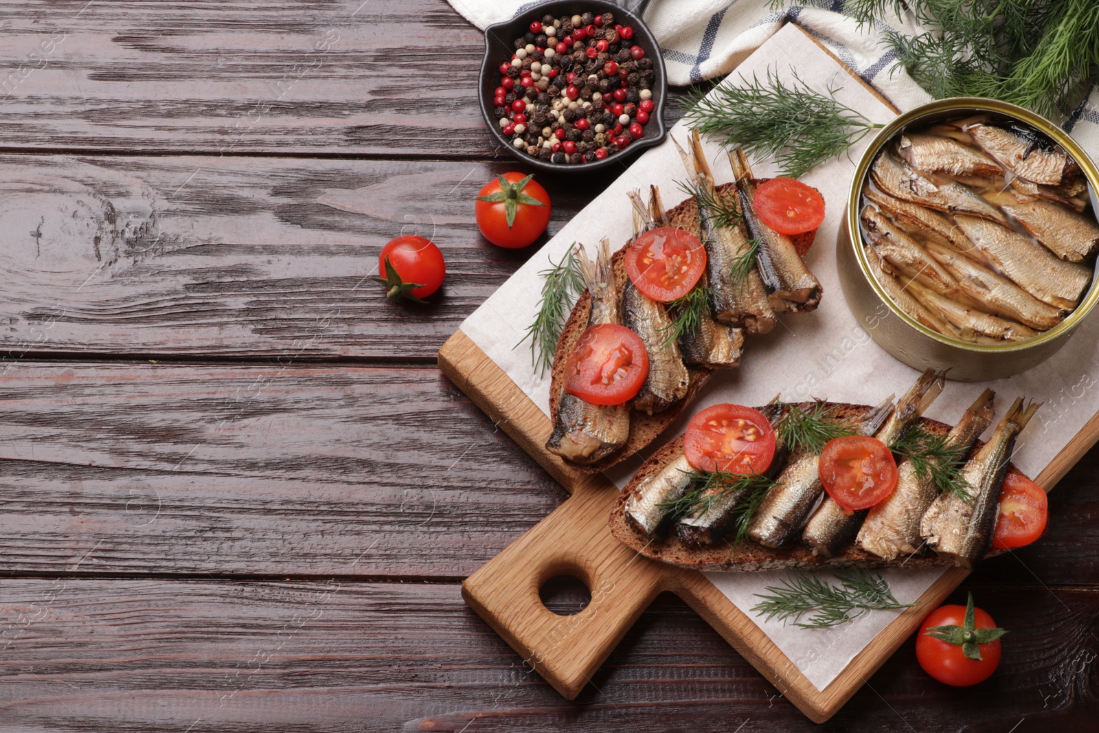 Photo of Delicious sandwiches with sprats, dill, tomatoes and peppercorns on wooden table, top view. Space for text