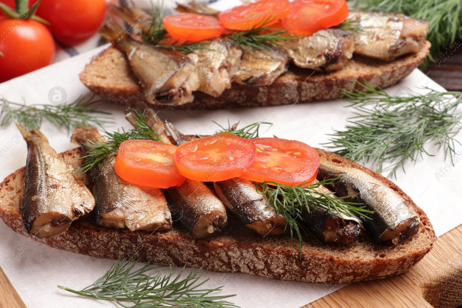 Photo of Delicious sandwiches with sprats, dill and tomato on table, closeup