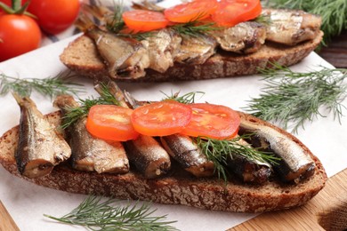 Photo of Delicious sandwiches with sprats, dill and tomato on table, closeup