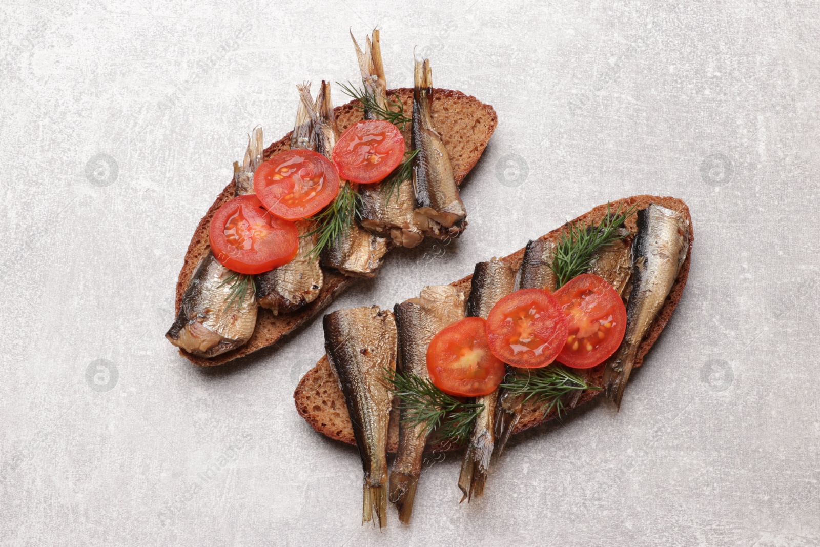 Photo of Delicious sandwiches with sprats, dill and tomato on grey table, top view