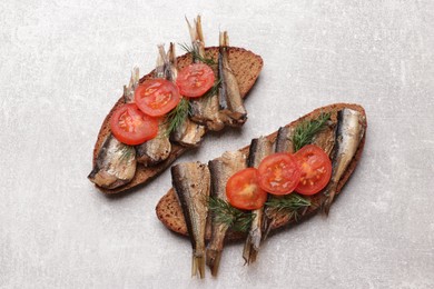 Delicious sandwiches with sprats, dill and tomato on grey table, top view