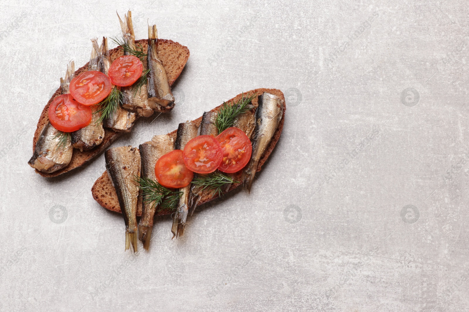 Photo of Delicious sandwiches with sprats, dill and tomato on grey table, top view. Space for text