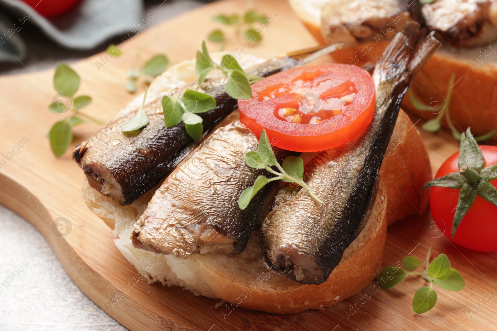 Photo of Delicious sandwich with sprats, microgreens and tomatoes on table, closeup