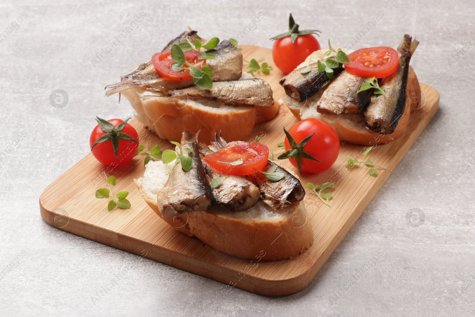 Photo of Delicious sandwiches with sprats, microgreens and tomatoes on grey table, closeup