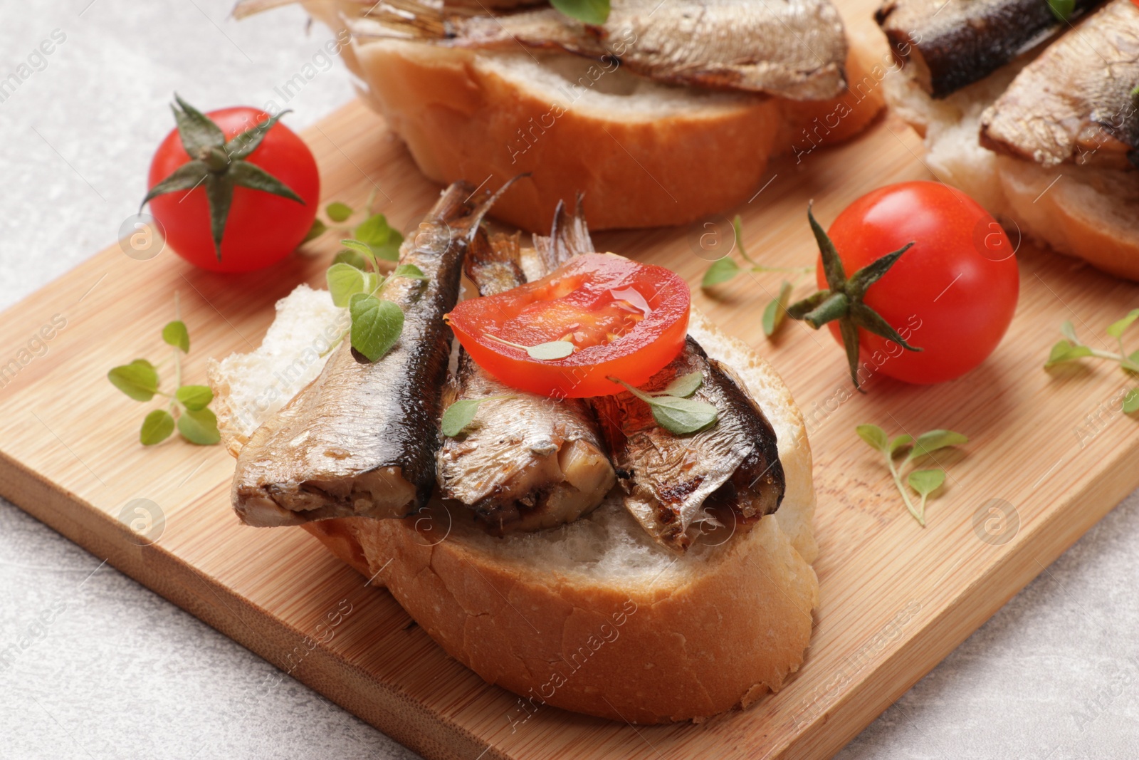 Photo of Delicious sandwiches with sprats, microgreens and tomatoes on grey table, closeup