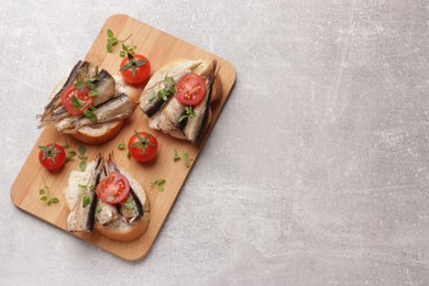 Photo of Delicious sandwiches with sprats, microgreens and tomatoes on grey table, top view. Space for text