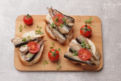 Photo of Delicious sandwiches with sprats, microgreens and tomatoes on grey table, top view