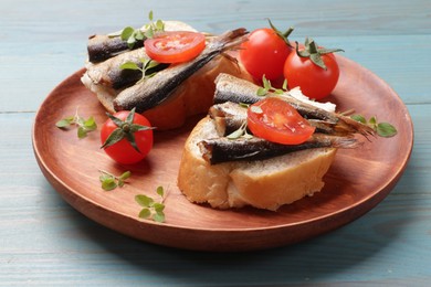 Delicious sandwiches with sprats, microgreens and tomatoes on light blue wooden table, closeup