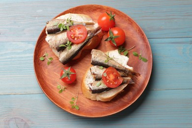 Photo of Delicious sandwiches with sprats, microgreens and tomatoes on light blue wooden table, top view