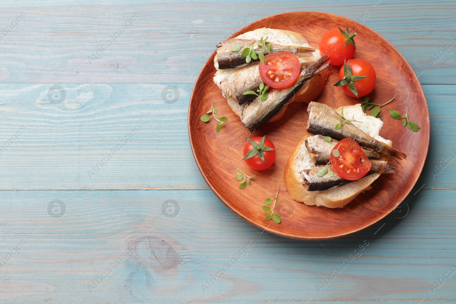 Photo of Delicious sandwiches with sprats, microgreens and tomatoes on light blue wooden table, top view. Space for text