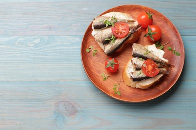 Photo of Delicious sandwiches with sprats, microgreens and tomatoes on light blue wooden table, top view. Space for text