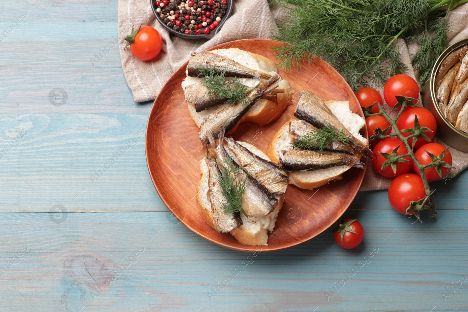 Photo of Delicious sandwiches with sprats and dill served on light blue wooden table, top view